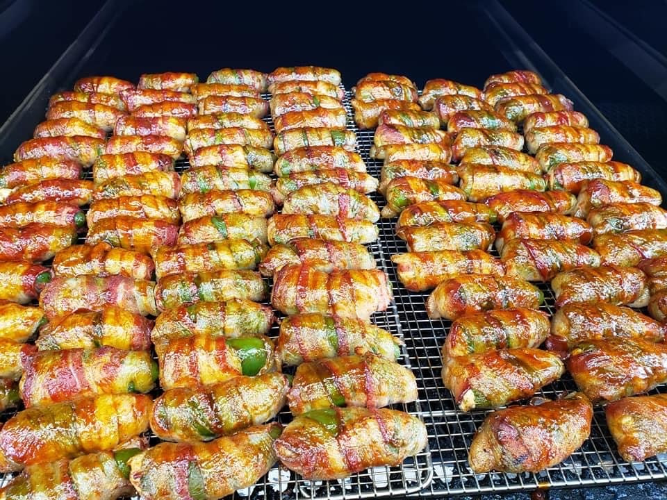 Rows of glazed bacon-wrapped jalapeño poppers cooking on racks inside a smoker.
