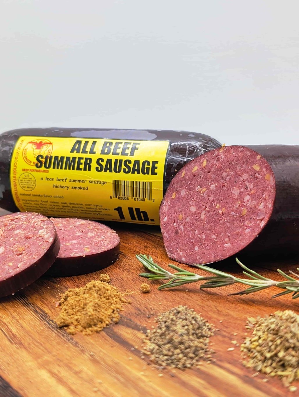 All Beef Summer Sausage on a wooden cutting board with spices and rosemary.