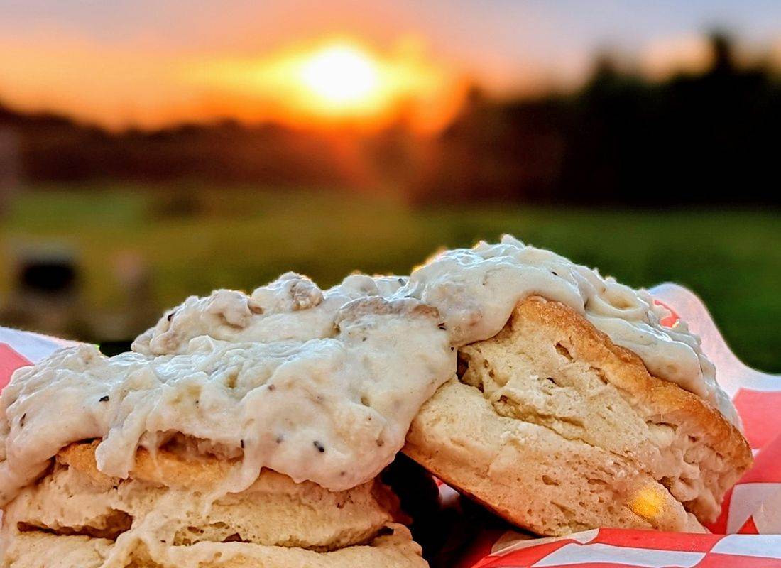 Fresh-baked biscuits covered in creamy sausage gravy with a glowing sunset in the background.