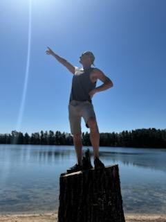 David Mauer, Vice President of Wisconsin River Meats, standing on a tree stump and pointing across a sunny Wisconsin lake.