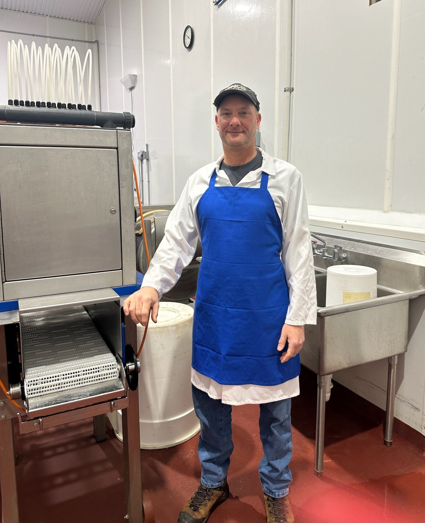 David Mauer, Vice President of Wisconsin River Meats, wearing a blue apron beside meat-processing equipment inside the facility.