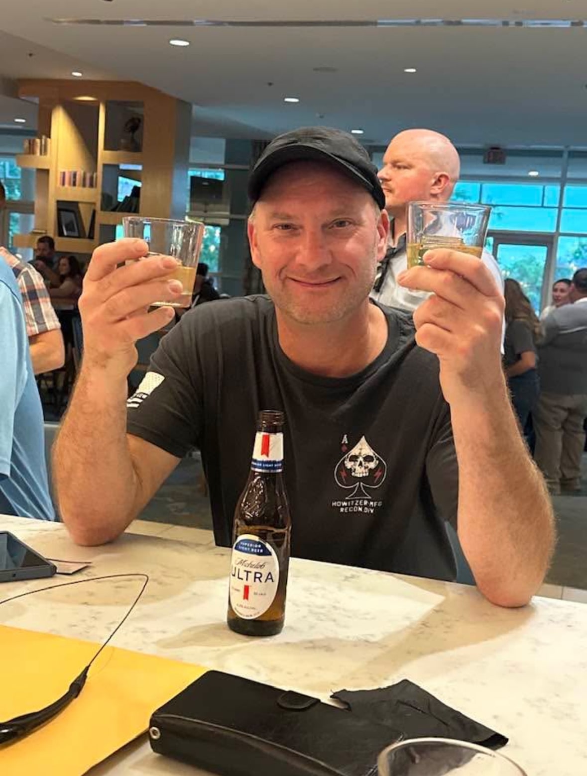 David Mauer, Vice President of Wisconsin River Meats, smiling and raising two glasses while seated at a crowded indoor event.