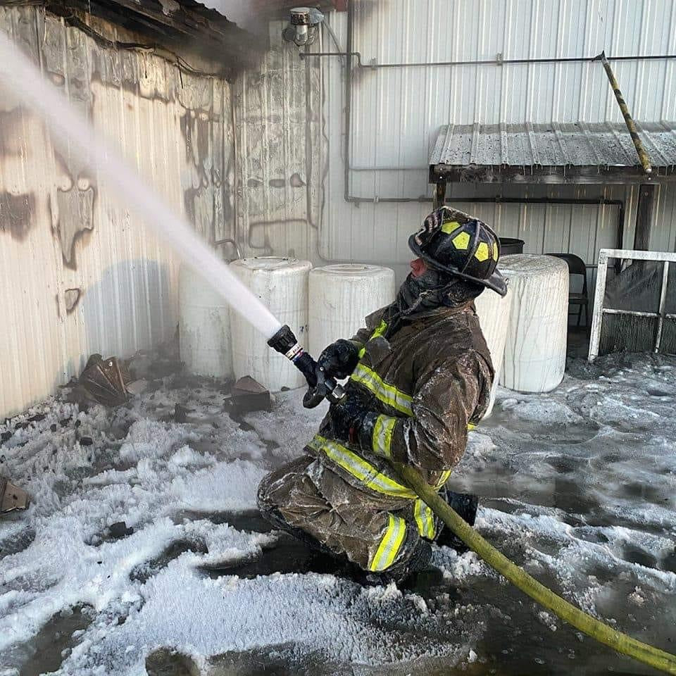 Firefighter spraying water inside the fire-damaged Wisconsin River Meats facility amid ice, foam, and smoke.