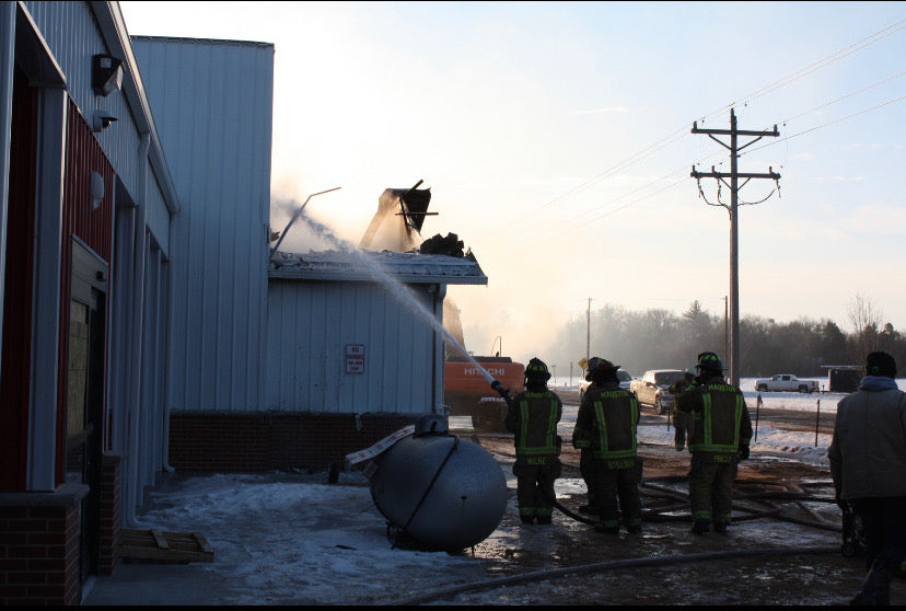 Mauston firefighters spraying water onto the smoking roof of the Wisconsin River Meats facility during a winter fire response.