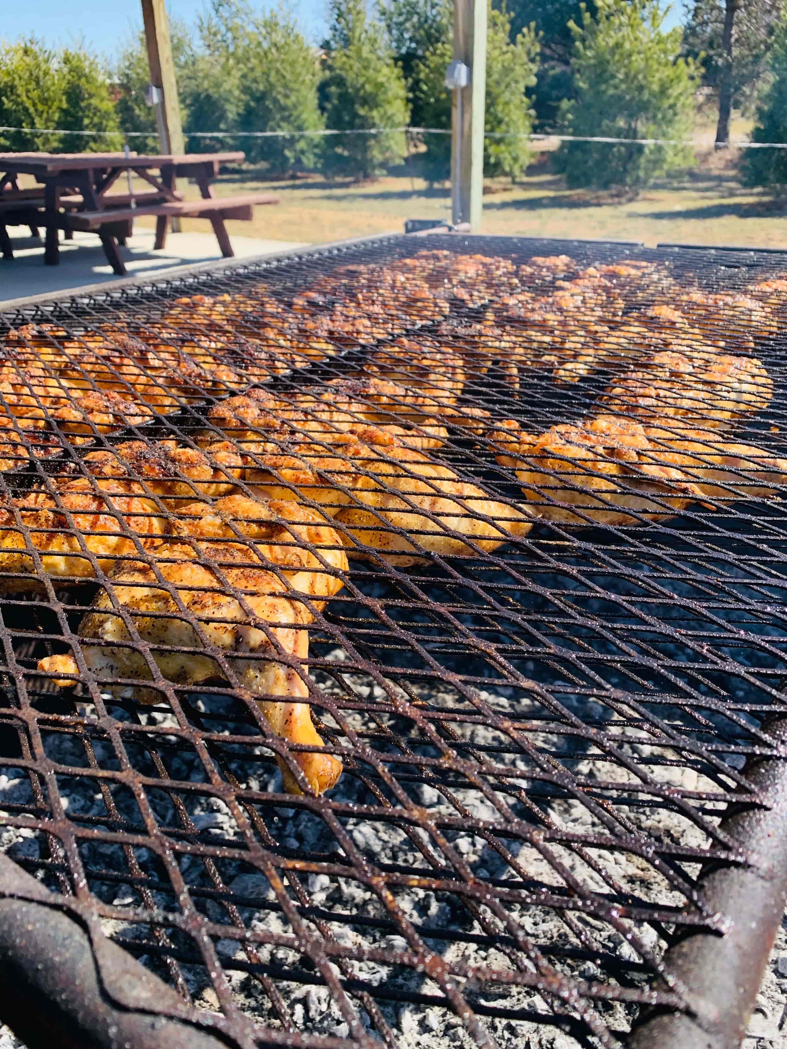 Seasoned chicken pieces cooking over charcoal on a large outdoor grill for a catered event.