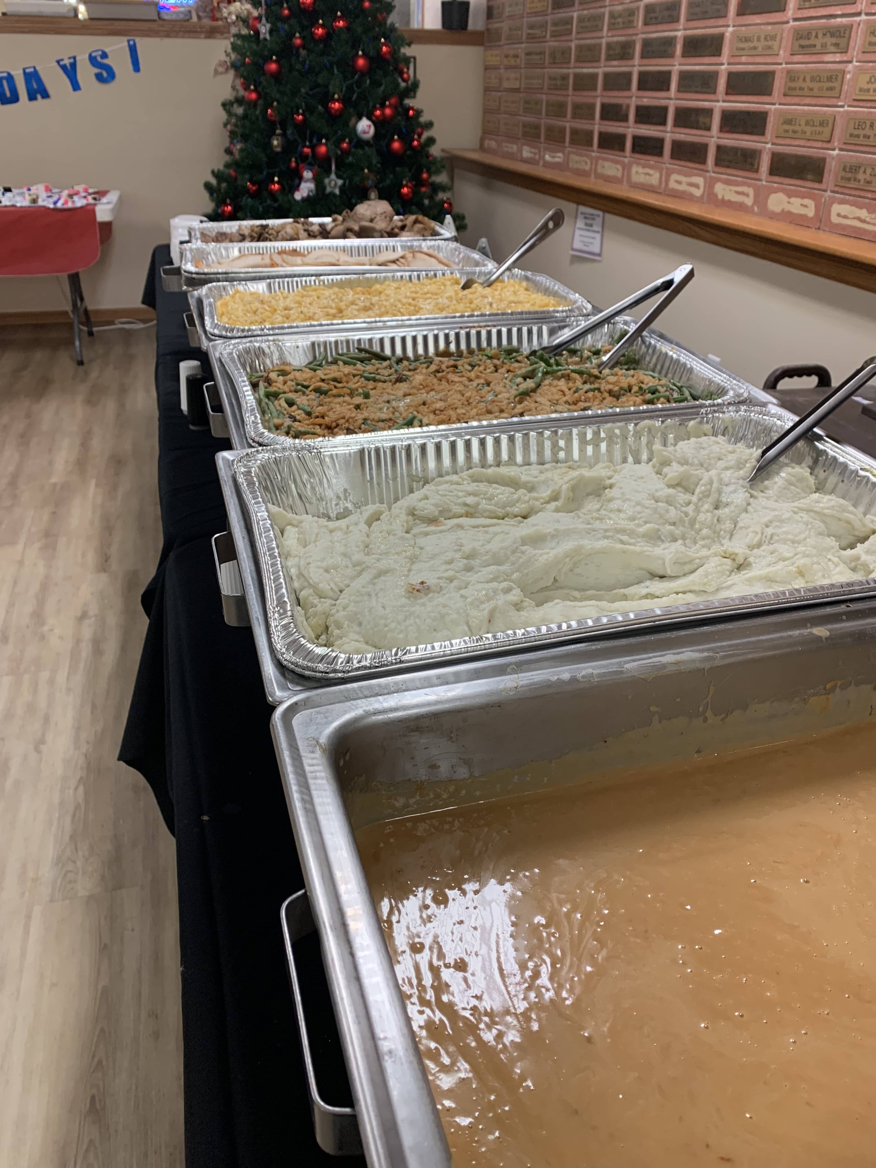 Holiday catering buffet with gravy, mashed potatoes, green bean casserole, macaroni and cheese, and sliced meats.