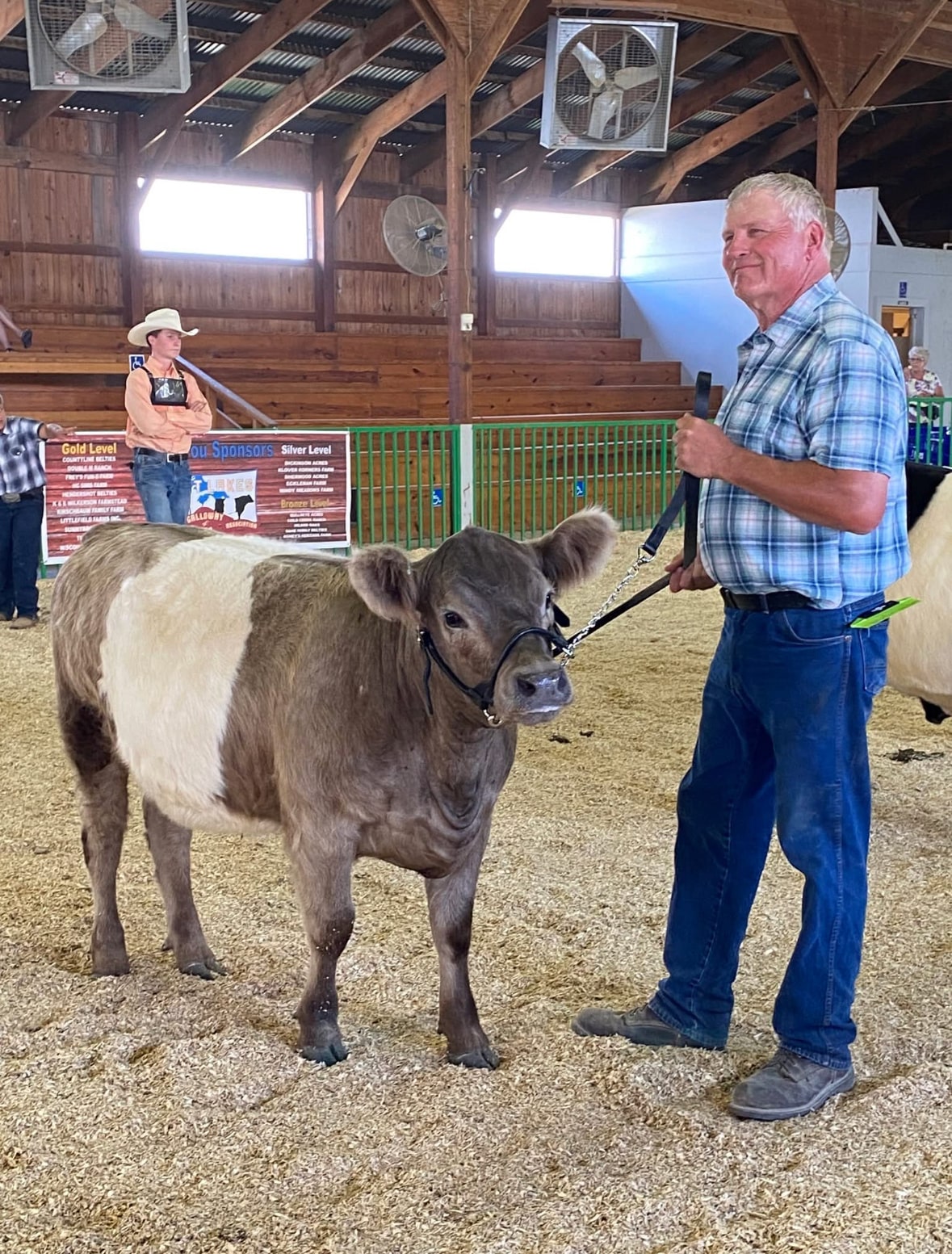 John Hamm, President of Wisconsin River Meats, standing beside a belted cow inside a livestock show barn.