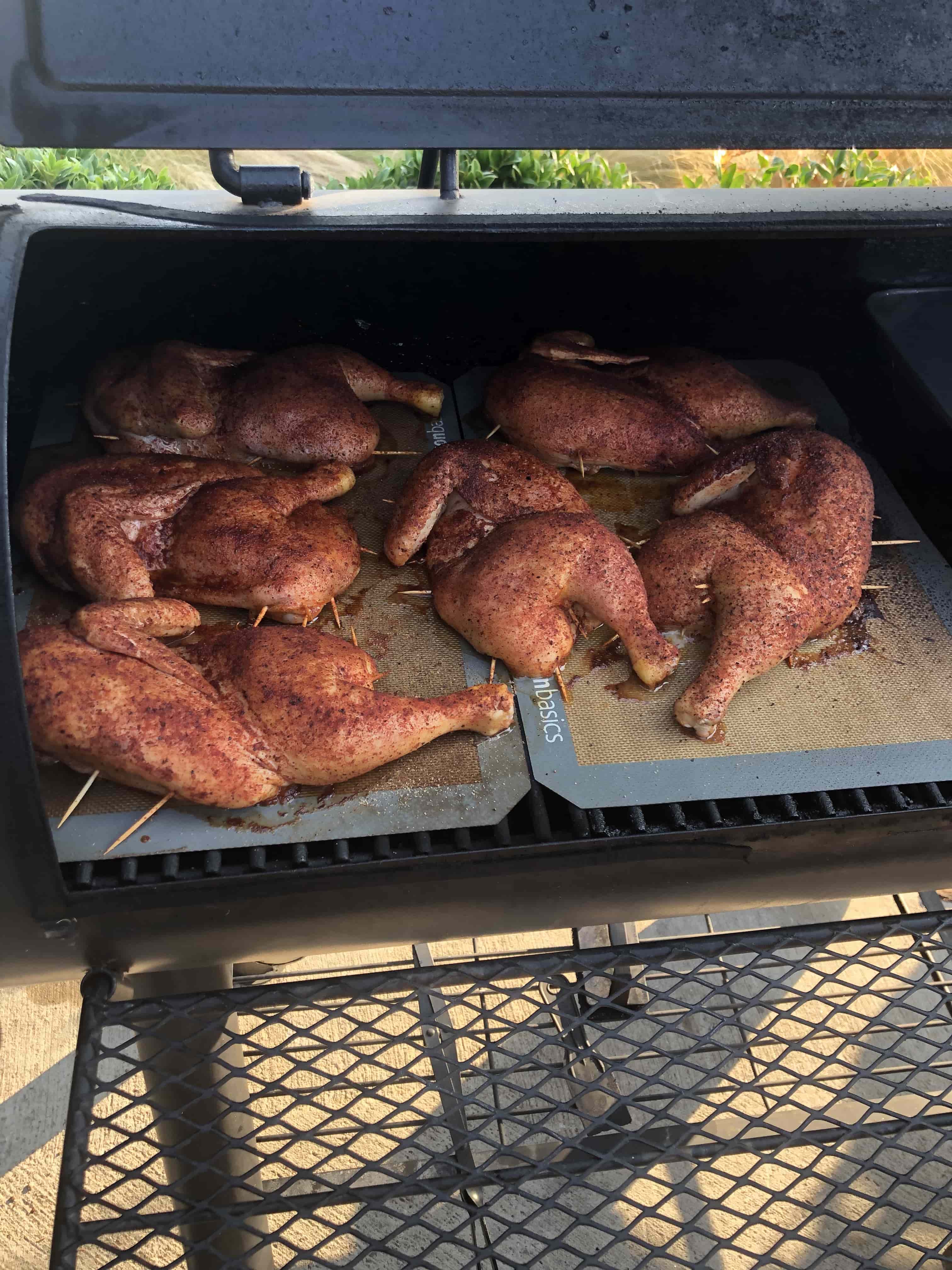 Seasoned chicken halves cooking inside a large outdoor smoker for a catered barbecue meal.